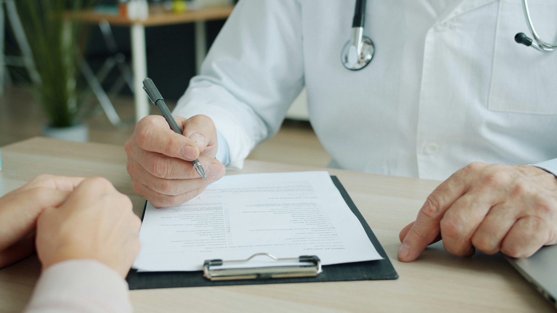 Un médico escribiendo en la historia clínica de un paciente.